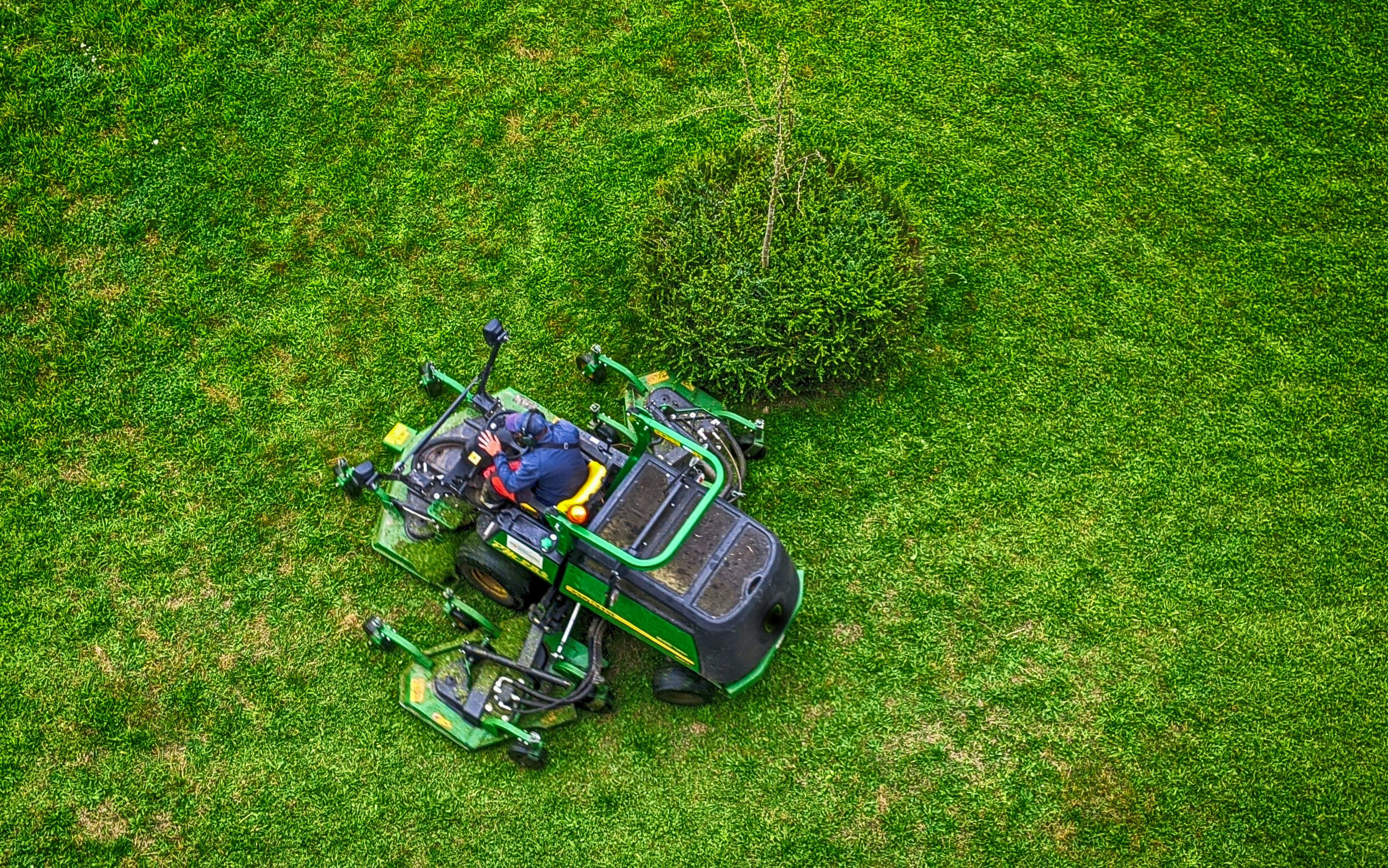 Person operating a green lawn mower on a grassy field